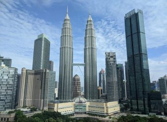Panoramic view of the iconic Petronas Towers in Kuala Lumpur against a blue sky.