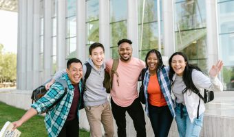 A happy group of diverse college students posing cheerfully outside a modern building.